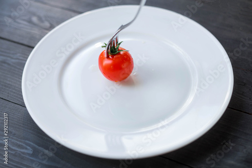 Cherry tomato lies in the middle of a white plate.