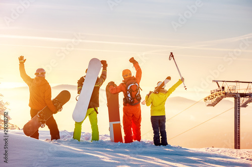 Happy skiers and snowboarders at sunset mountain top