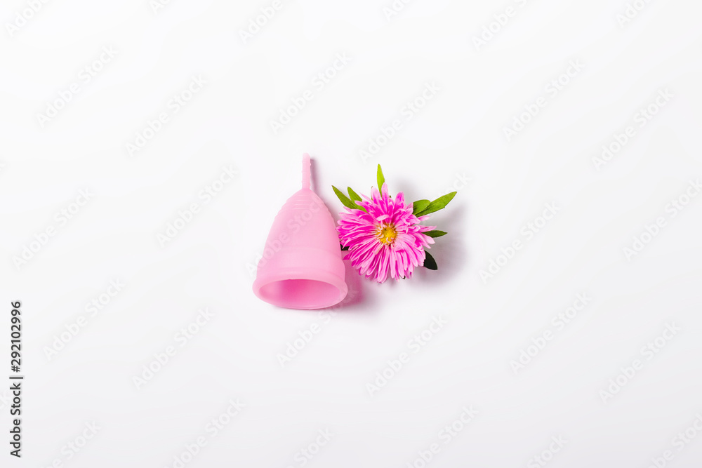 Pink menstrual cup and flower on a white background. Concept of menstruation, the choice between feminine hygiene products. Flat lay, top