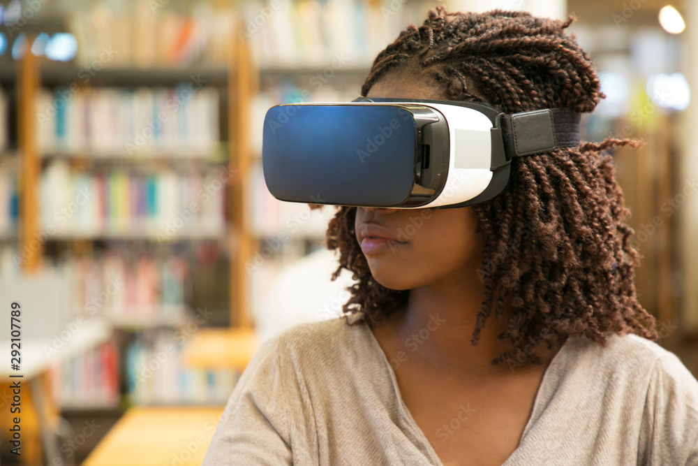 African American student girl using VR glasses for work in library. Young  black woman wearing virtual reality headset, sitting at desk. VR technology  concept foto de Stock | Adobe Stock