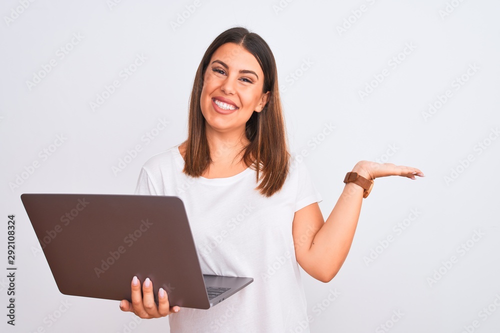 Beautiful young woman working using computer laptop over white background smiling cheerful presenting and pointing with palm of hand looking at the camera. Beautiful young woman working using computer laptop over white background smiling cheerful presenting and pointing with palm of hand looking at the camera.