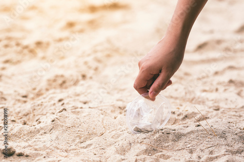 A hand cleaning and picking up a plastic glass trash on the beach