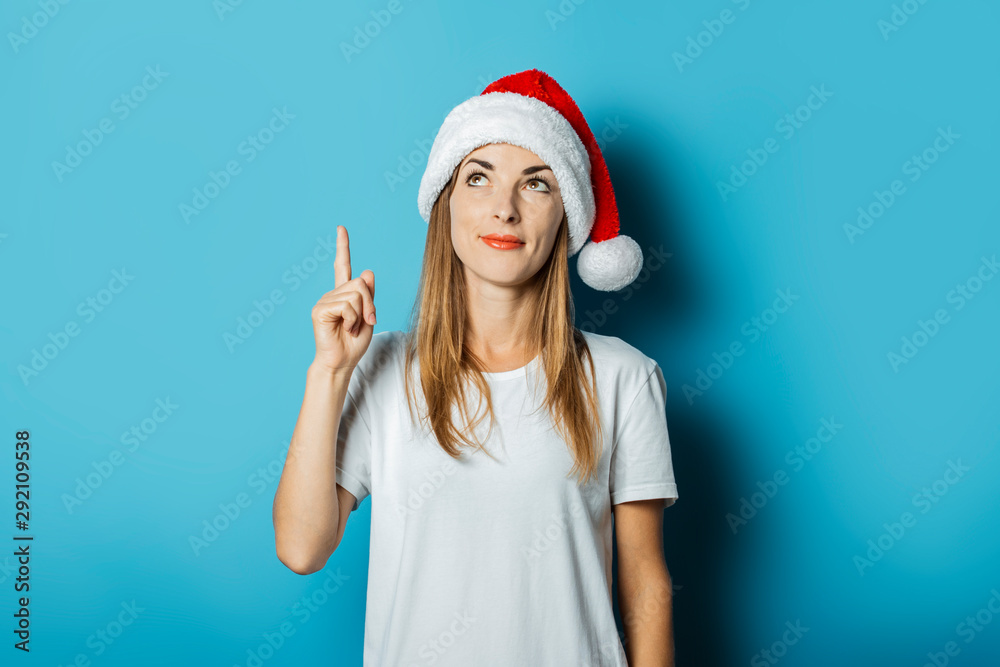 Young woman in Santa Claus hat with a mysterious face on a blue background. Concept idea for new year and christmas