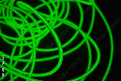 Toxic green luminous wires with different shapes and structures. A web of lime fiber and unusual circles located on a black glossy surface.