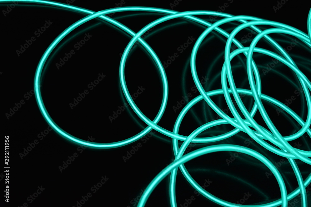 Unusual bright wires made of turquoise-colored material glowing at night. Chaotic sky blue wires, light guide electroluminescent wires, electroluminescence are located on a glossy black surface. Unusual bright wires made of turquoise-colored material glowing at night. Chaotic sky blue wires, light guide electroluminescent wires, electroluminescence are located on a glossy black surface.