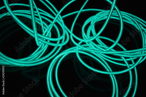 Unusual bright wires made of turquoise-colored material glowing at night. Chaotic sky blue wires, light guide electroluminescent wires, electroluminescence are located on a glossy black surface.