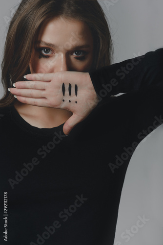 A crying young girl covering her mouth with her palm, on which there are three exclamation marks.