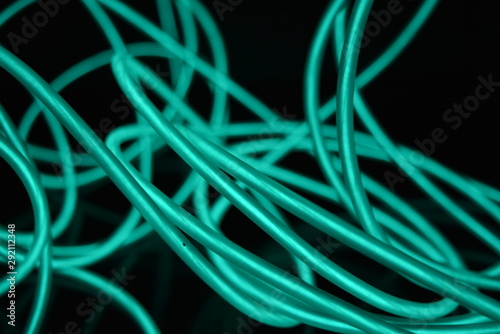 Unusual bright wires made of turquoise-colored material glowing at night. Chaotic sky blue wires  light guide electroluminescent wires  electroluminescence are located on a glossy black surface.