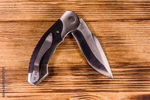 Opened folding knife on a wooden table. Top view