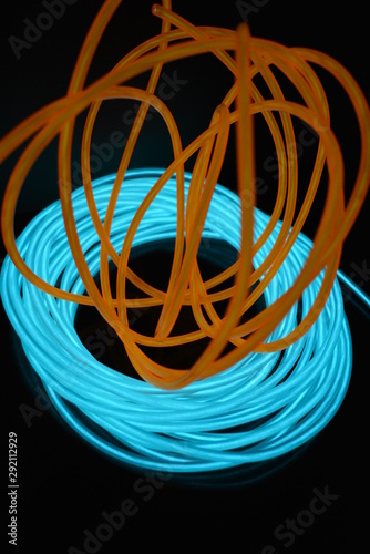 A bright coil of turquoise  sky blue luminous wire with chaotic wires of an orange light guide located on a black glossy surface. Light canvas  backlighting with wires and art background.