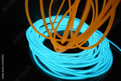 A bright coil of turquoise  sky blue luminous wire with chaotic wires of an orange light guide located on a black glossy surface. Light canvas  backlighting with wires and art background.