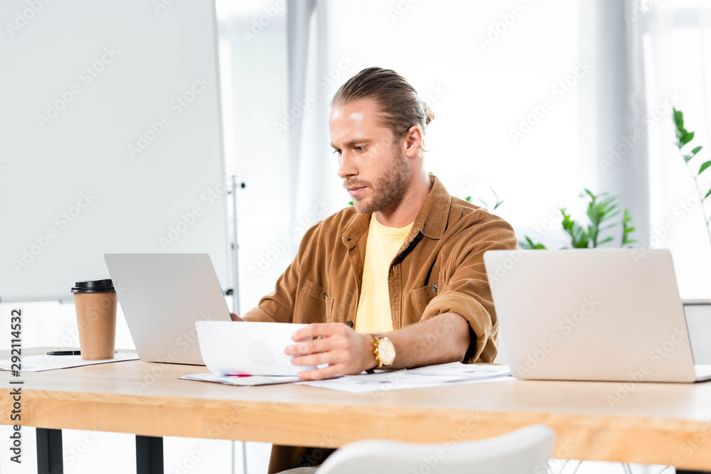 handsome man doing paperwork and looking at laptop handsome man doing paperwork and looking at laptop
