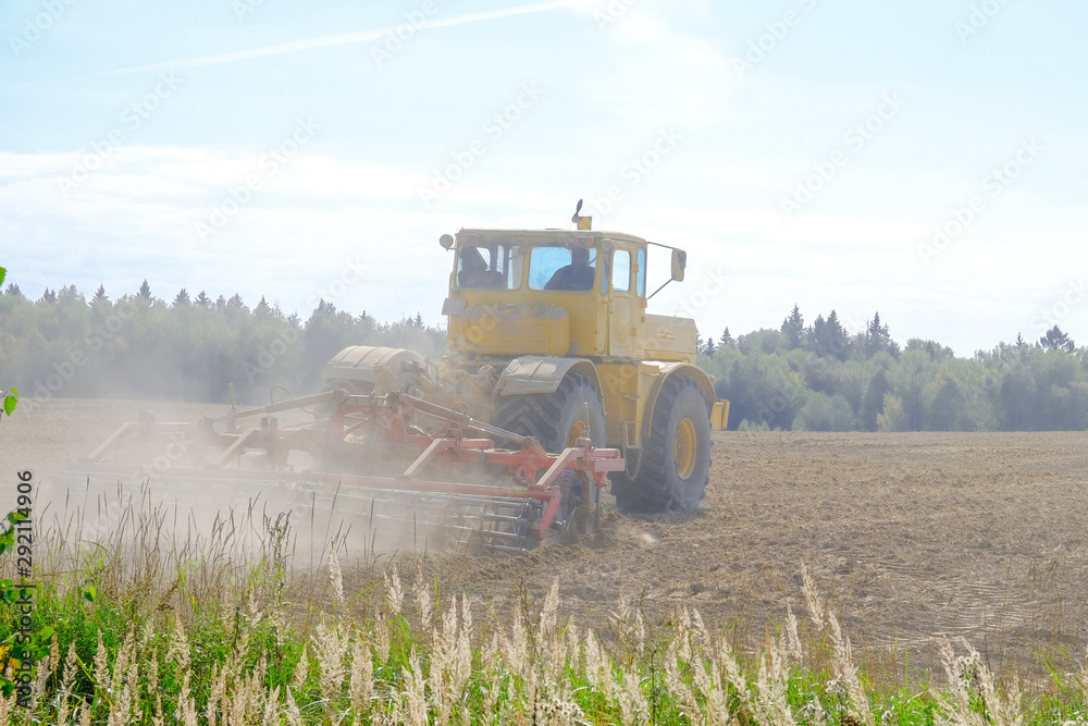 Fototapeta premium A farm tractor cultivates land after harvesting grain.