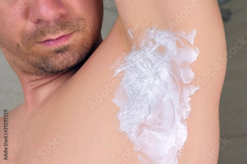 Depilation cream on armpit of young man, closeup view. Concept of cosmetic hygienic procedure making at home. Male shaving underarm in shower. Waiting few minutes to wash out cream. photo