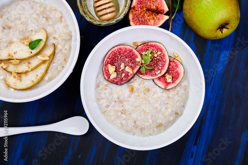 A bowl of porridge with pears slices and walnuts and porridge with figs on dark blue background. Two bowls. Flat lay. Copy space. Top view.