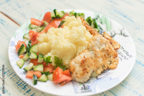 Mashed potatoes with chop and fresh vegetable salad in a plate on wooden background.