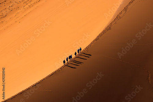 Aerial view group of people walking on the sand dune in the desert and sun gradually create beautiful scene.