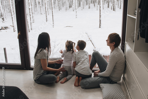 The family is sitting at the window and looking at the winter forest. Good New Year spirit. Morning in pajamas.