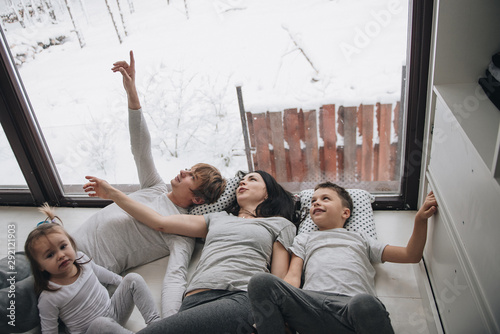 The family is sitting at the window and looking at the winter forest. Good New Year spirit. Morning in pajamas.