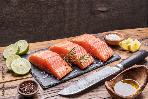 Fresh salmon fillets on black cutting board with herbs and spices.