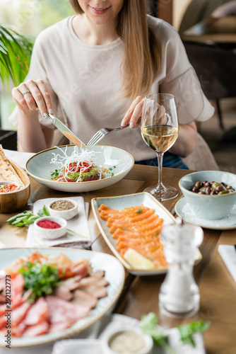 Portrait of a beautiful young elegant woman in the restaurant with a wine glass. Dinner and a variety of dishes on the table. Italian cuisine