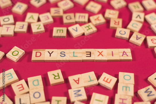 high angle view of a wooden alphabet blocks with DYSLEXIA word in the center on pink background. Concept of Dyslexia awareness and human brain development photo