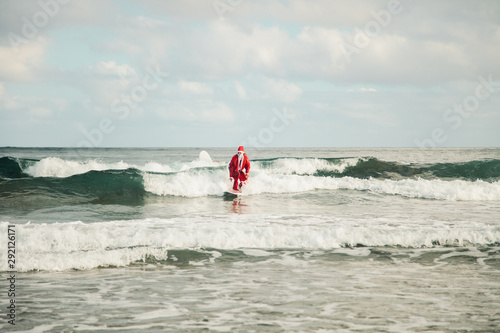 Young man surfer dressed as Santa Claus on the beach