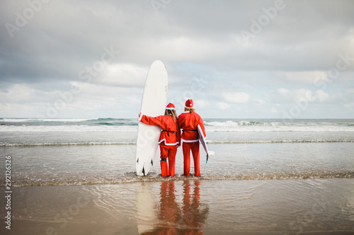 two surfers dressed as Santa Claus on the beach