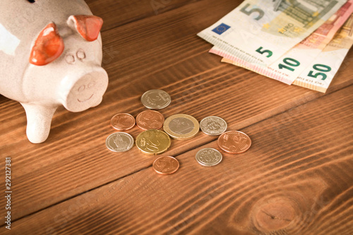 Piggy Bank and a few coins and Euro bills on the wooden table. Close up. The concept of saving money. Selective focus.