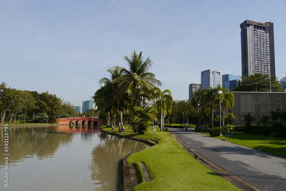 Tropischer Park mit Teich, Palmen und Hochhäusern in Bangkok