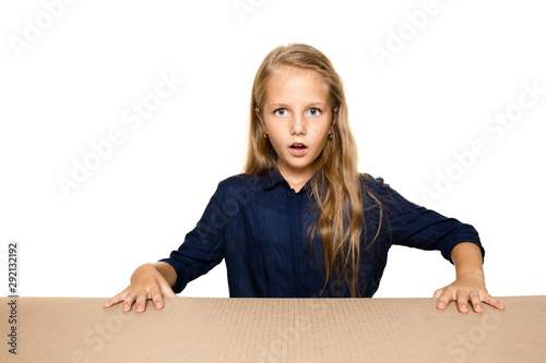 Cute and astonished little girl opening the biggest postal package. Excited young female model on top of cardboard box looking inside. Gift, present, delivery, shipment, sales, black friday concept.