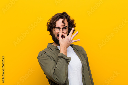 Obraz na plátne young crazy man feeling disgusted, holding nose to avoid smelling a foul and unp