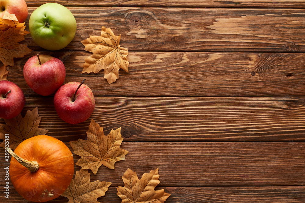 top view of small pumpkin and apples on brown wooden surface with dried autumn leaves top view of small pumpkin and apples on brown wooden surface with dried autumn leaves
