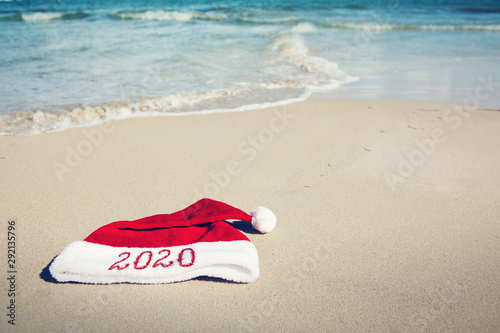 Year 2020 written at the Santa Claus hat on caribbean beach. New Year background