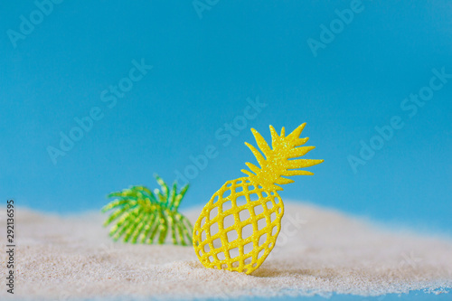 Close-up of bright yellow lace pineapple and green leaves on the sand beach.