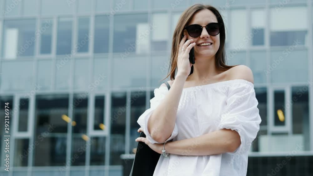 Modern and happy young businesswoman speak by mobile phone and smiling, business center in the background Modern and happy young businesswoman speak by mobile phone and smiling, business center in the background