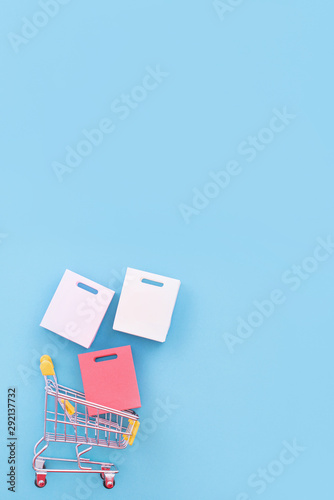 Abstract design element, concept of annual sale, shopping season - mini yellow cart with paper bag isolated on pastel blue background, top view, flat lay.