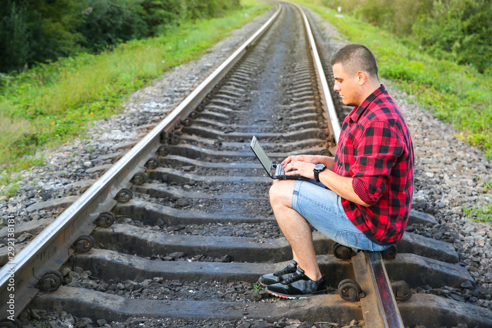 Guy with a laptop is sitting on the railway tracks. Freelance hipster worker. Man is working traveling. Guy with a laptop is sitting on the railway tracks. Freelance hipster worker. Man is working traveling.