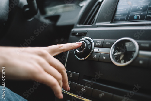 Close up photo of a female finger that reaches out to turn on the multimedia system. Selective focus. Listening music in the auto. Power button. Car clock. Interior of automobile. Travelling by car. 