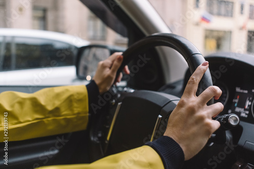 Close up photo of unrecognizable girl, who drive car by two hands. Journey concept. Selective focus on right arm. Yellow jacket. Blurred background. Travelling by automobile. Comfort transportation.