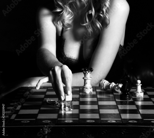 Seductive woman in lace lingerie with deep neckline playing chess with perfume bottles, pointing one photo