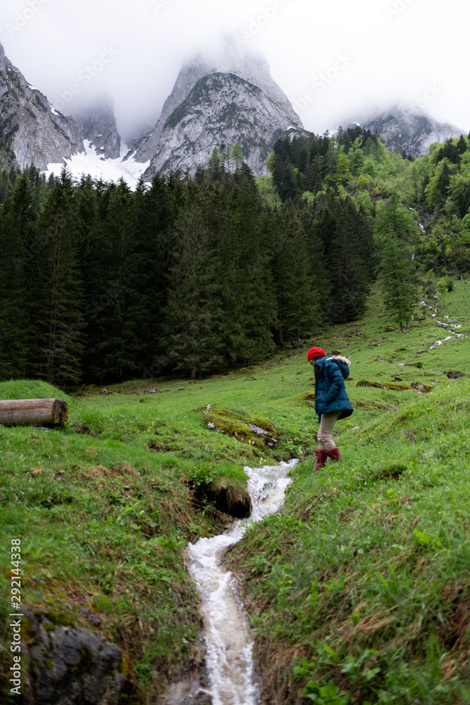 Asian woman with red hat clambing the rock at small water stream with background of mountain and forest.