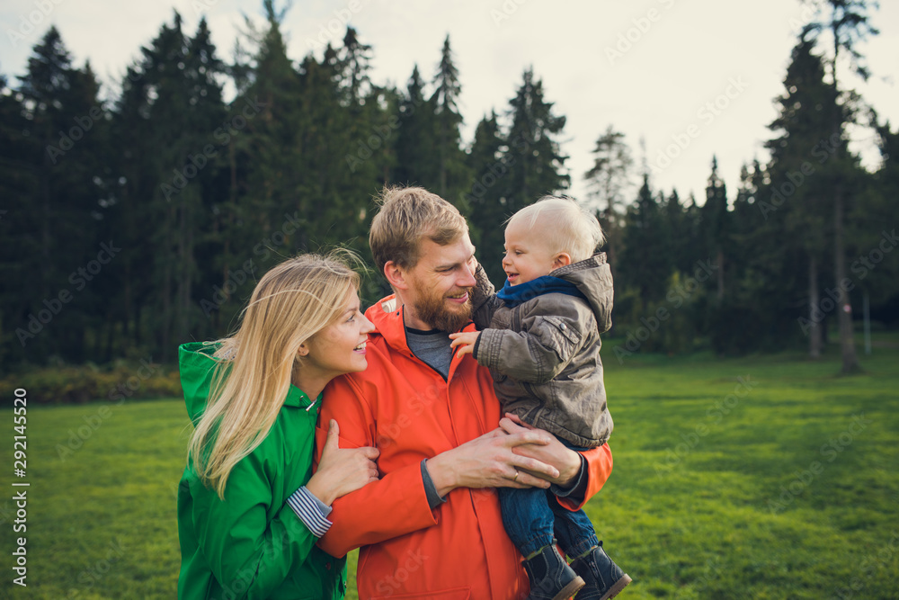 happy parents hold little son and laugh, lifestyle family portrait outdoors
