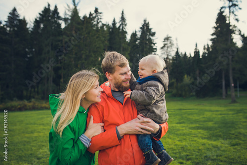 happy parents hold little son and laugh, lifestyle family portrait outdoors