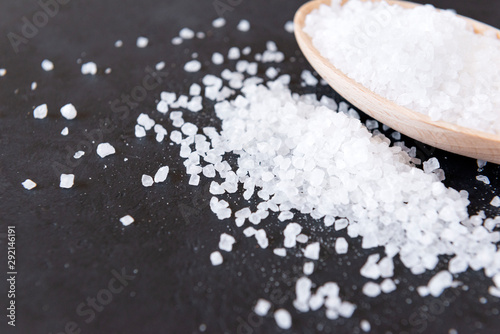 granules of coarse salt in a wooden spoon and scattered on a black background
