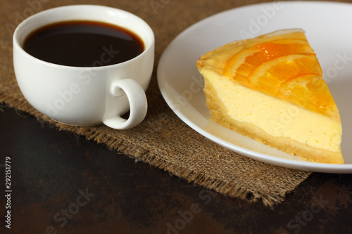 Cheesecake with oranges and a mug of coffee on burlap tablecloth.