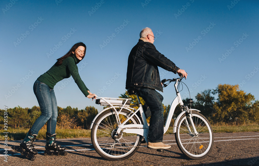 Obraz premium Young girl on roller skates and a man on a electric bike fun ride together. Active leisure and hobbies. Father and daughter.