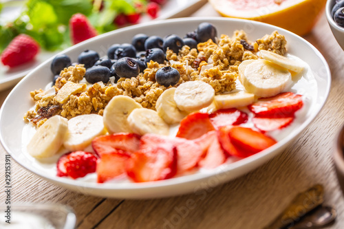 Healthy breakfast served with plate of yogurt muesli blueberries strawberries and banana.