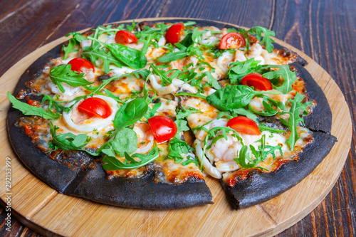 Pizza on black dough with arugula and cherry