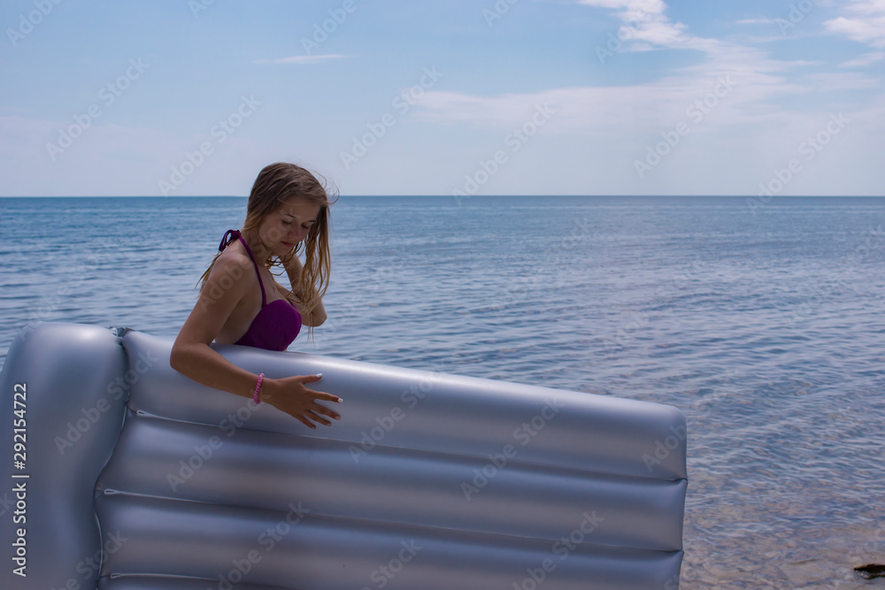 fascinating young girl in swimsuit and with air mattress on the beach